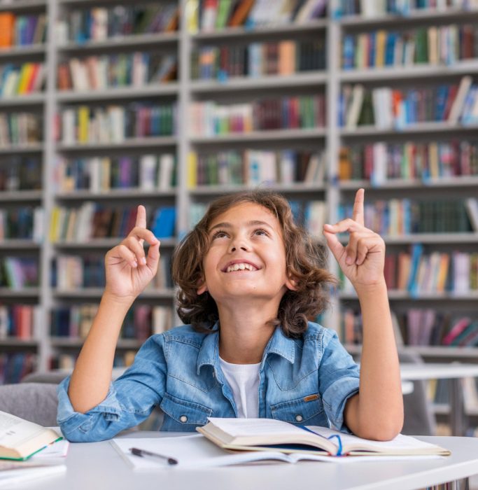 Happy school student studying in a library with books.
